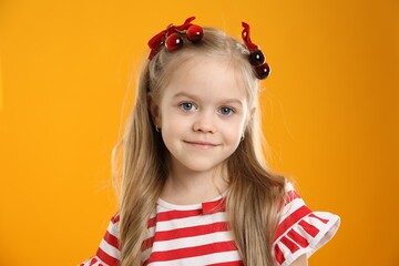Cute little girl wearing beautiful bows with cherries on orange background