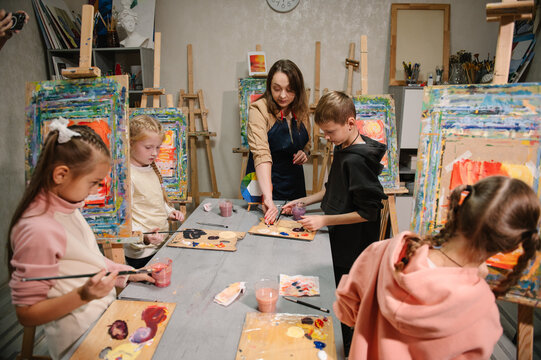 Childs painting in workshop. Artist explains how to mix and combine colors. Kids drawing brush on easel. Education, learning concept.  Teacher learn children to draw pictures in an art lesson. - Powered by Adobe