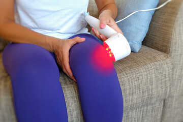 A woman uses an innovative red light therapy device on her knee to effectively relieve pain and relieve inflammation of the injured knee