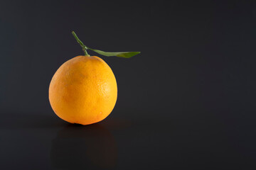 A fresh, rich and healthy orange with leaf resting on black background