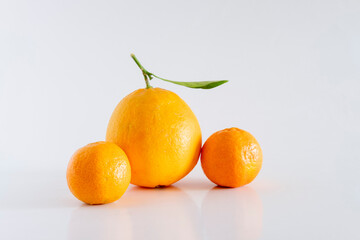 A fresh, rich and healthy orange and several tangerines with leaf resting on white background