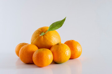 A fresh, rich and healthy orange and several tangerines with leaf resting on white background