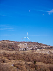 Modern wind power generator on rural hillside. Sustainable energy technology: wind turbine on mountain with road below