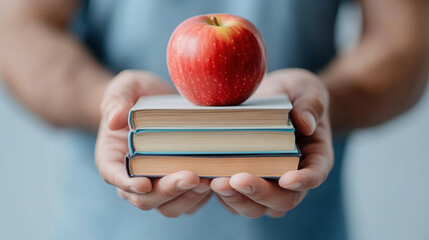 Person holding stack of books with red apple on top