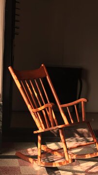 The rocking chair rocks or moves in the room. The sun shines on the rocking chair for elderly people. It is comfortable furniture.