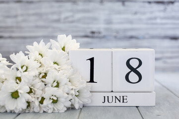 White wood calendar blocks with the date June 18th and white daisies. Selective focus with blurred background. 