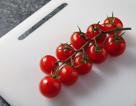 A vibrant cluster of cherry tomatoes on the vine placed on a smooth white cutting board