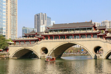 Fototapeta premium Little wooden boat passing through the arch of the ancient Anshun Lang Bridge in Chengdu, on the Jinjiang River. Sichuan, China