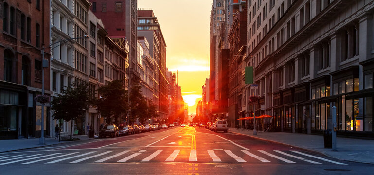 Empty streets and sidewalks at 5th Avenue and 23rd St in New York City with sunset shining between the background buildings of the Manhattan cityscape