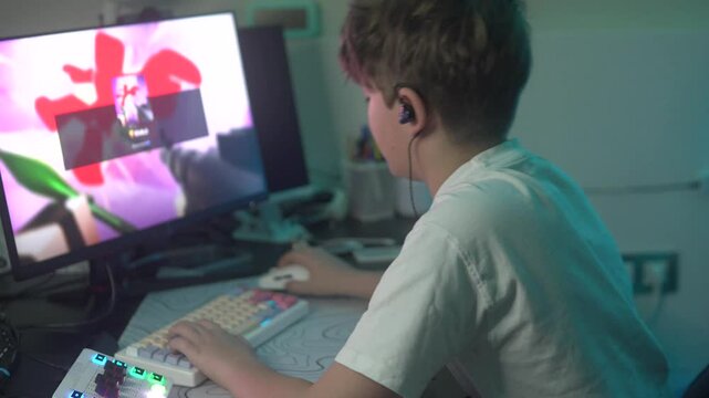 A boy is playing a computer game in a dark room