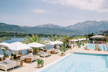 Double sun loungers with sun umbrellas stand on the shore of the pool by the sea
