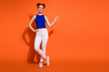 Young woman in a stylish outfit smiling while gesturing against bright orange background, exuding energy and elegance