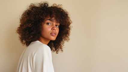 Junge Frau mit voluminösem Afro-Haar in hellem Oberteil vor beiger Wand im Porträt