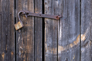 old wooden door locked with rusty padlock. vintage gate to building locked with bolt