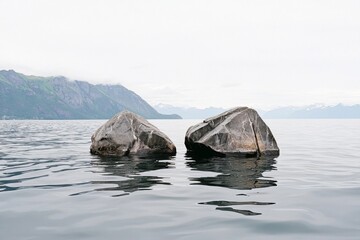Two large rocks emerging from calm water with mountains in the background