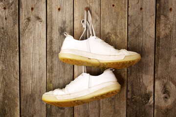 White sport shoes hanging from laces on a rustic wooden wall