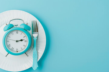Clock on a plate with a fork, concept: intermittent fasting, dieting, and meal timing, concept of intermittent fasting, controlled meal timing, or dieting