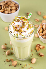 Pistachio milkshake, healthy diet protein cocktail, non-dairy whipped shake with vegan pistachio milk, whipped plant-based cream, sprinkled with nuts, on light green background