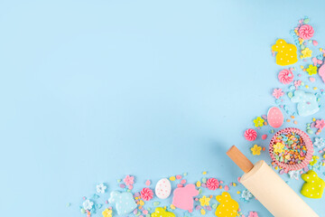 Easter baking background with sugar sprinkles, sugar Easter bunny, easter egg and spring flowers decoration, rolling pin and bakery accessories, light blue background top view copy space