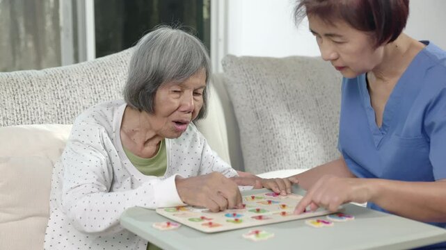Nurse in nursing home helping elderly woman play number puzzle game. Dementia, Alzheimer's disease.