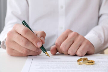Man signing marriage contract and wedding rings on desk, closeup