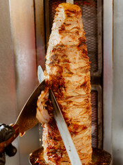 Gyros or doner, Middle East traditional food. Man's hands holding a knife, cutting slices from a vertical skewer