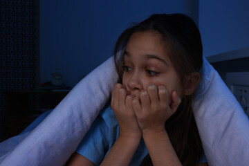 Afraid girl hiding under duvet on bed at night