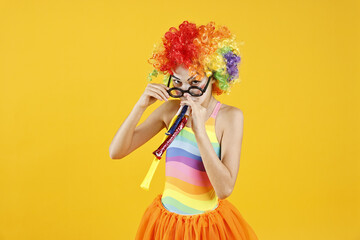 Girl dressed like clown with blowers on yellow background. Surprise party