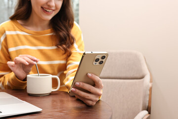 Smiling woman with smartphone having coffee break in cafe, closeup. Space for text