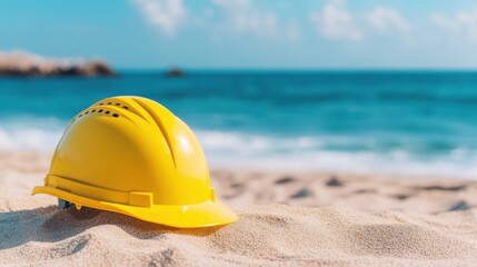 A yellow hard hat rests on sandy beach, contrasting with the vibrant blue ocean and clear sky, symbolizing construction and leisure.