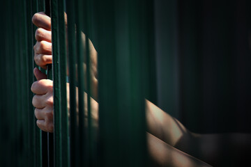 Hands Gripping Metal Bars in Dim Light Illustrating Confinement