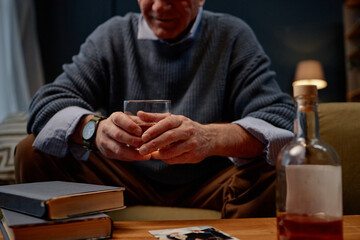Elderly man enjoying an evening with a glass of whiskey, sitting surrounded by books and a bottle beside him, creating a warm and reflective atmosphere