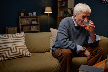 Senior man wearing sweater and drinking beverage while seated on comfortable sofa in cozy living...