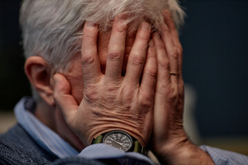 Elderly individual is holding face in hands, showing wristwatch and wearing a sweater, creating an...