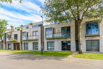 Obraz premium Row of new terraced houses with glass rooftop decks along a street on a sunny summer day