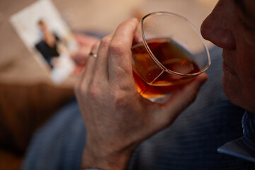 Close-up of hand holding glass of whiskey with blurred photograph in background capturing intimate moment. Focus on glass and hand with person in suit
