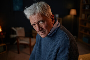 Portrait of elderly man with gray hair and serious expression in a cozy, dimly lit room with...