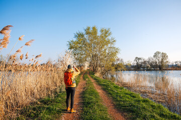 Tourist with binoculars observes birds arriving at lake in springtime. Birdwatching and wildlife...