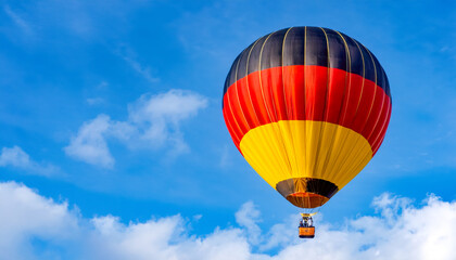 Fototapeta premium Colorful hot air balloon floats against a clear blue sky in a vibrant display of yellow, black, and red