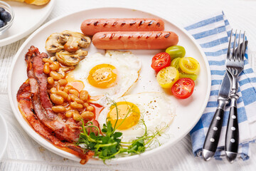 A classic breakfast plate featuring sunny-side-up eggs, crispy bacon, sausages, and fresh tomatoes