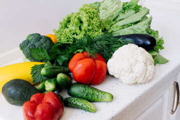 Fresh vegetables on a white kitchen table (zucchini, avocado, lettuce, cauliflower, cucumber, bell pepper, eggplant, broccoli, dill)