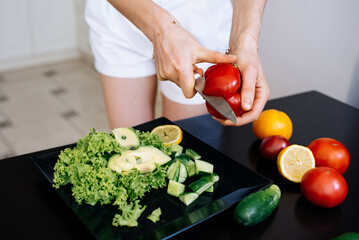 female hands cutting bell pepper for salad on a background of a tray with vegetables