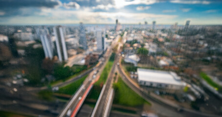 Blurred background of a large city with wide avenues, tall and low-density buildings seen through watermarked glass of a window