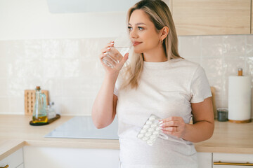 Young beautiful pregnant woman drinking water with vitamins at home in the kitchen.