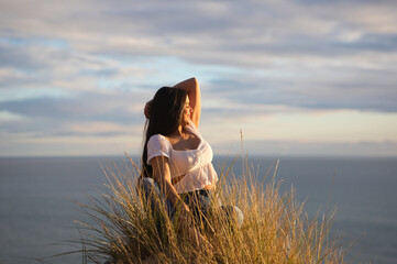 Young and beautiful Latin woman, brunette, sitting on a fine white sand dune among the reeds. The...