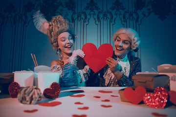 Elegant couple in baroque attire holding red heart in aristocratic setting with modern interior...