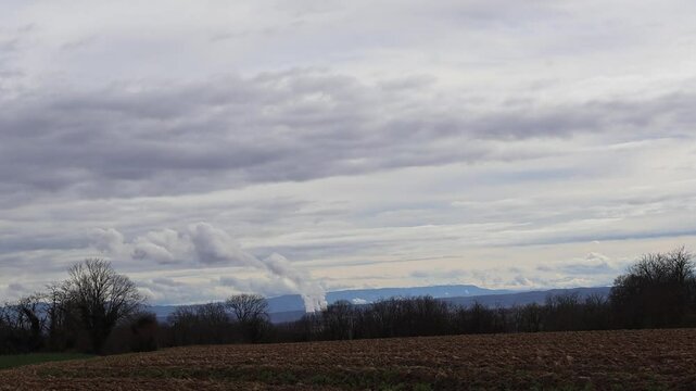 Vue panoramique de Montluel : champs, for&ecirc;t, ciel nuageux et fum&eacute;e au loin de la centrale de Saint Vulbas.