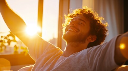 A young man waking up in bed, stretching his arms with a relaxed smile as warm morning sunlight streams through the window.
