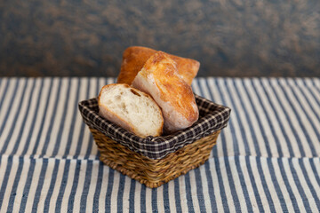 A basket of freshly baked artisan bread with a golden crispy crust and airy interior, placed on a blue-and-white striped fabric. Rustic homemade bread, perfect for breakfast or a cozy meal.