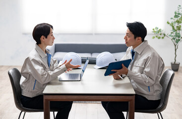 ミーティングをする作業着を着たミドルの男女